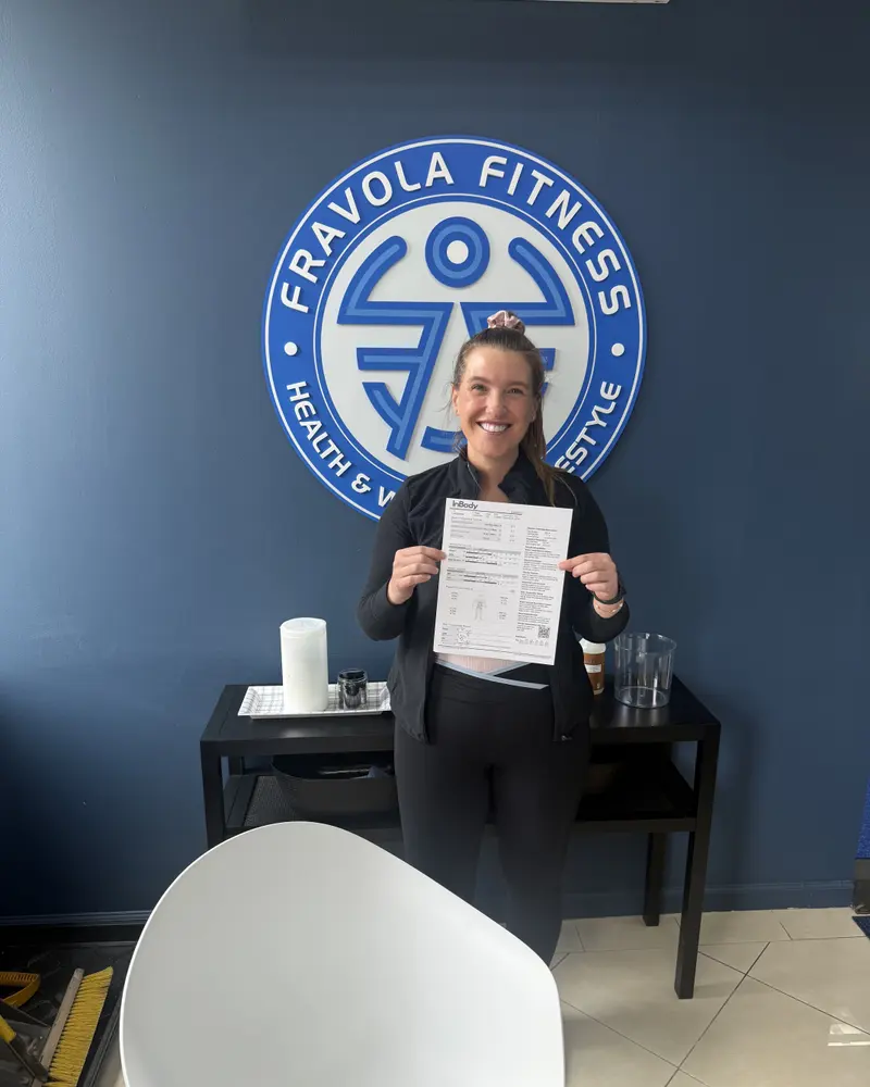 A member with their results in front of the Fravola Fitness logo wall
